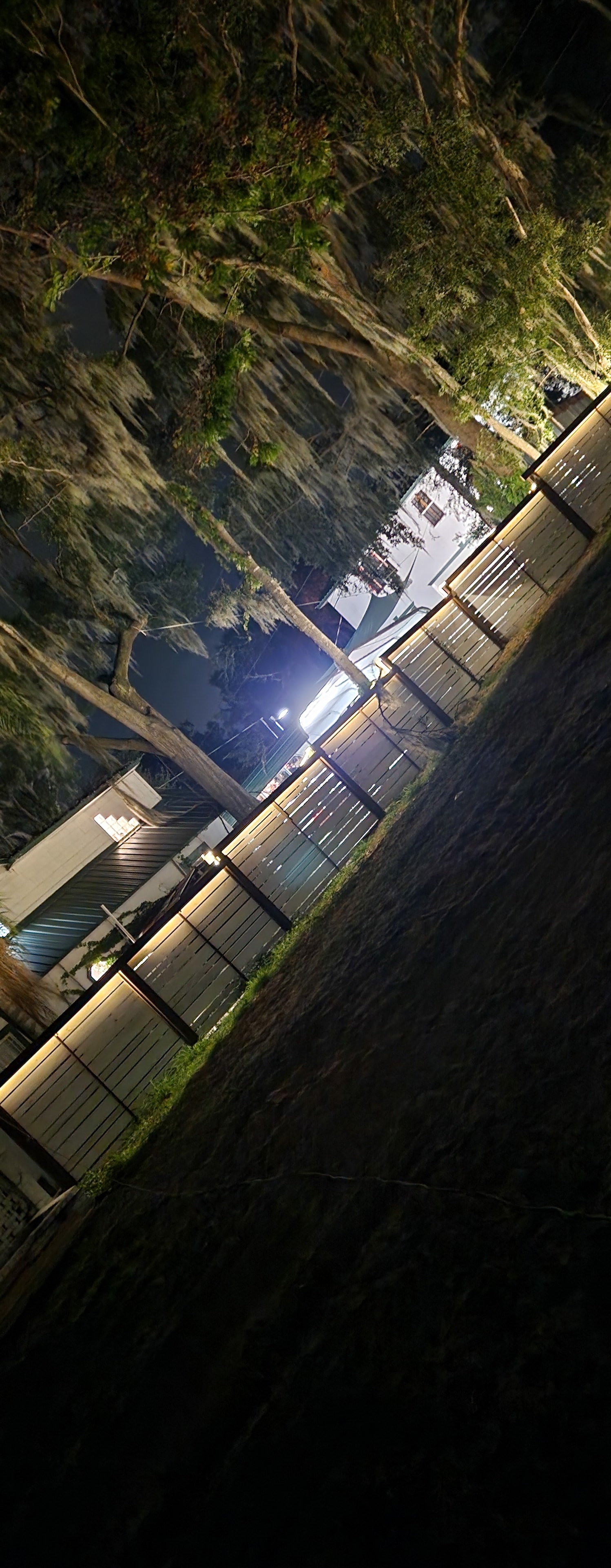 Aerial nighttime photograph of a completed horizontal fence and deck structure with landscape lighting.