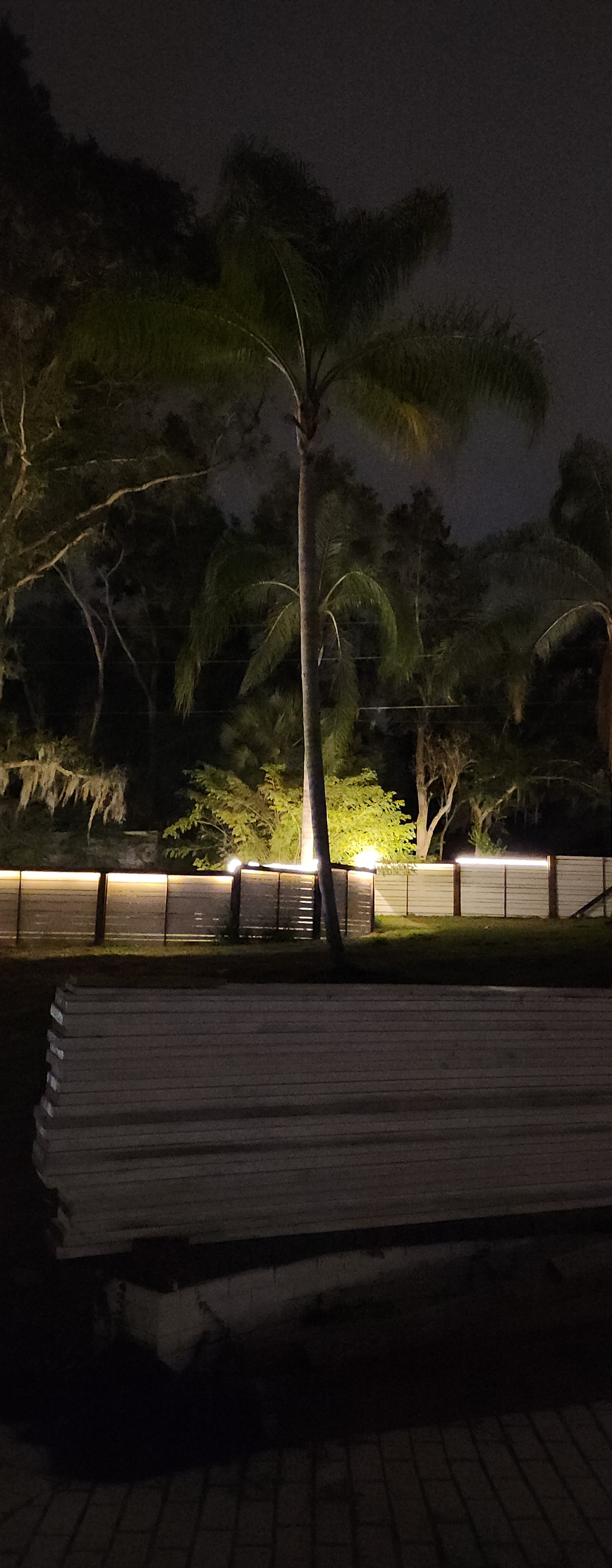 Custom deck feature with illuminated glass rock and crystal planter bed surrounding a mature tree at night.