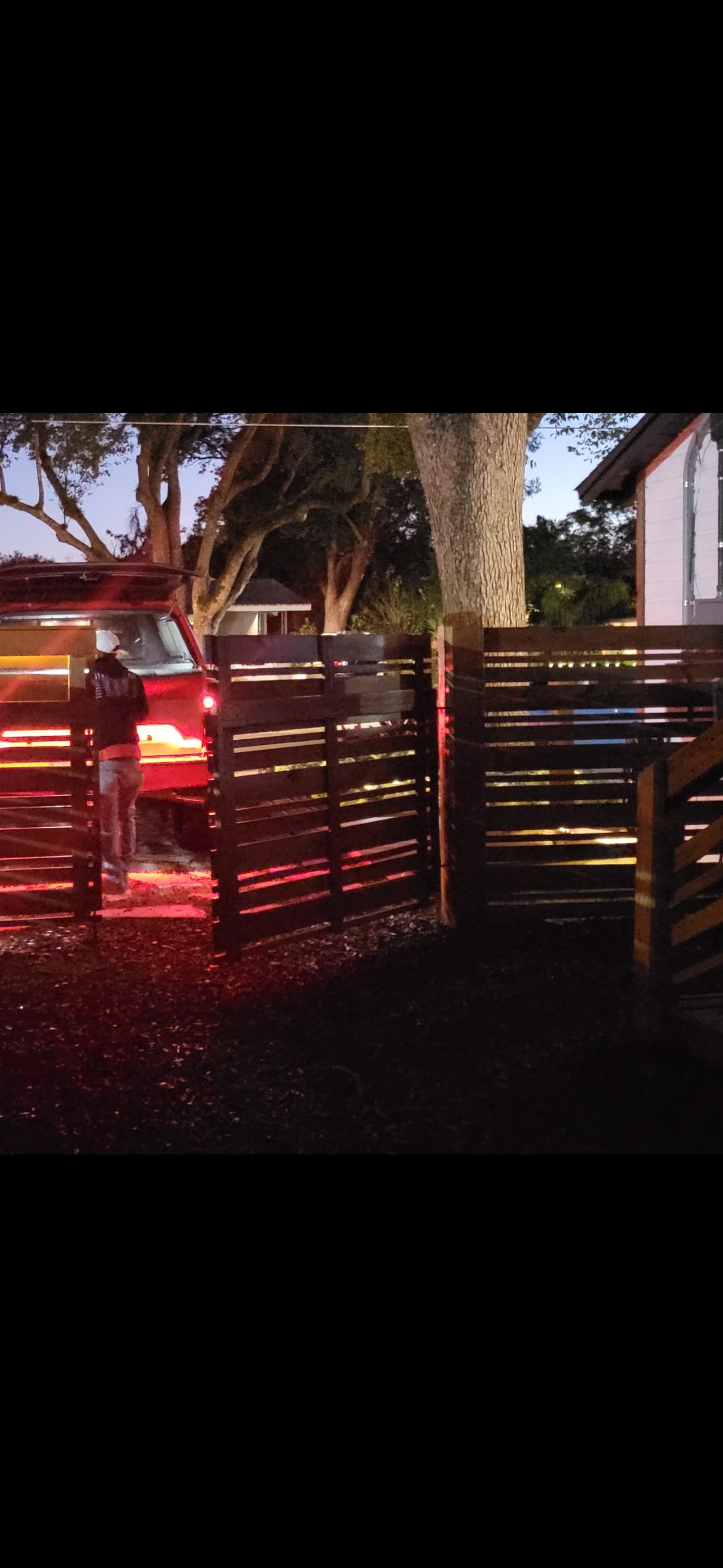 Red Star truck parked at a custom horizontal fence gate at dusk, showcasing the finished fencing project.