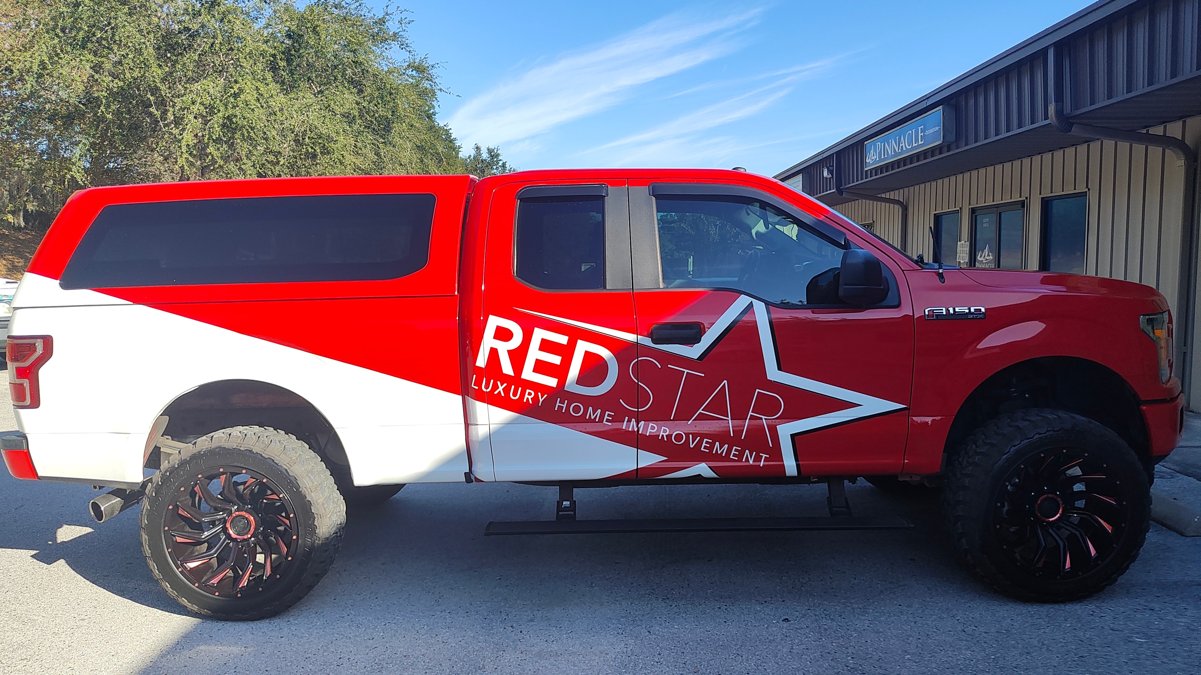 The Red Star Luxury Home Improvement F-150 with red and white custom wrap and star logo, parked at a commercial location.