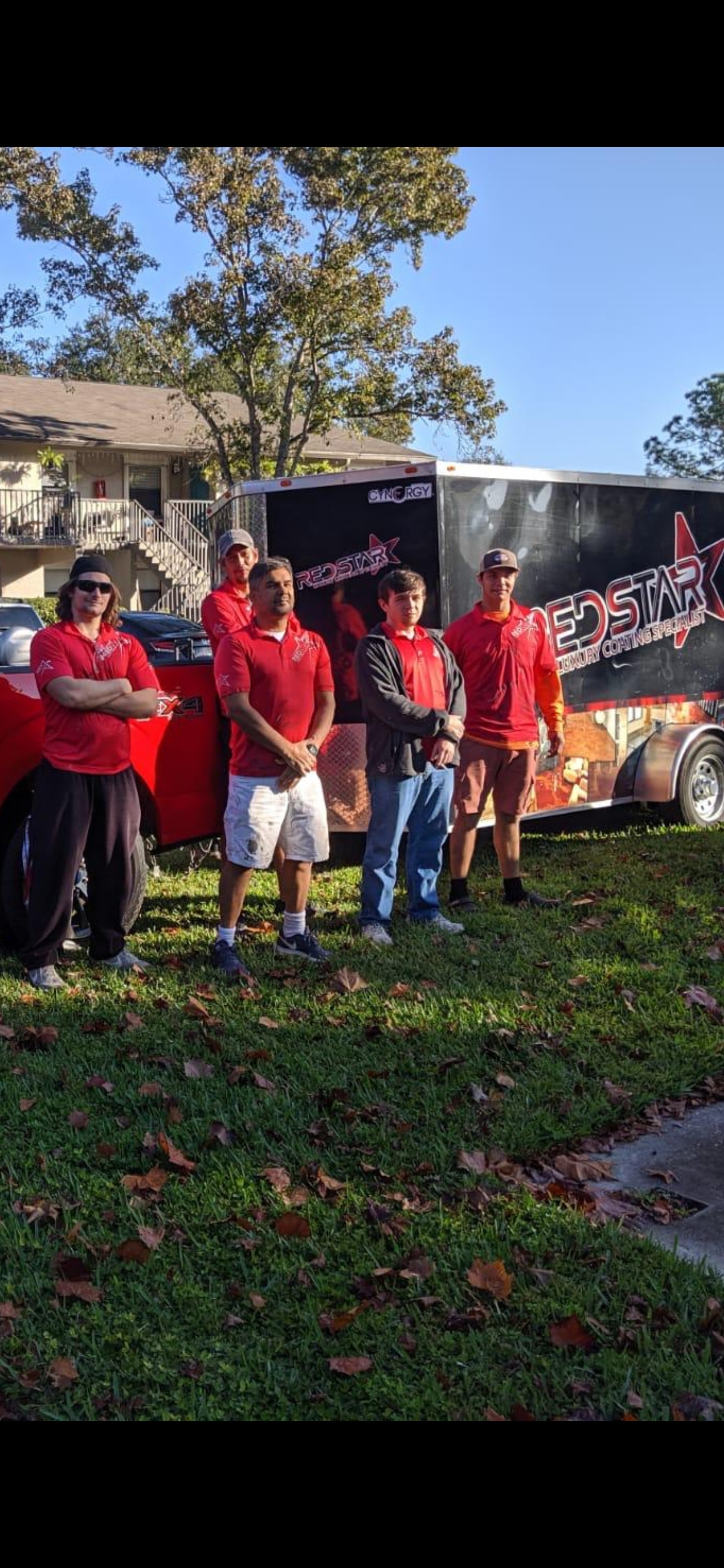 Five Red Star team members in red branded shirts standing in front of the Red Star Luxury Coating Specialist trailer.